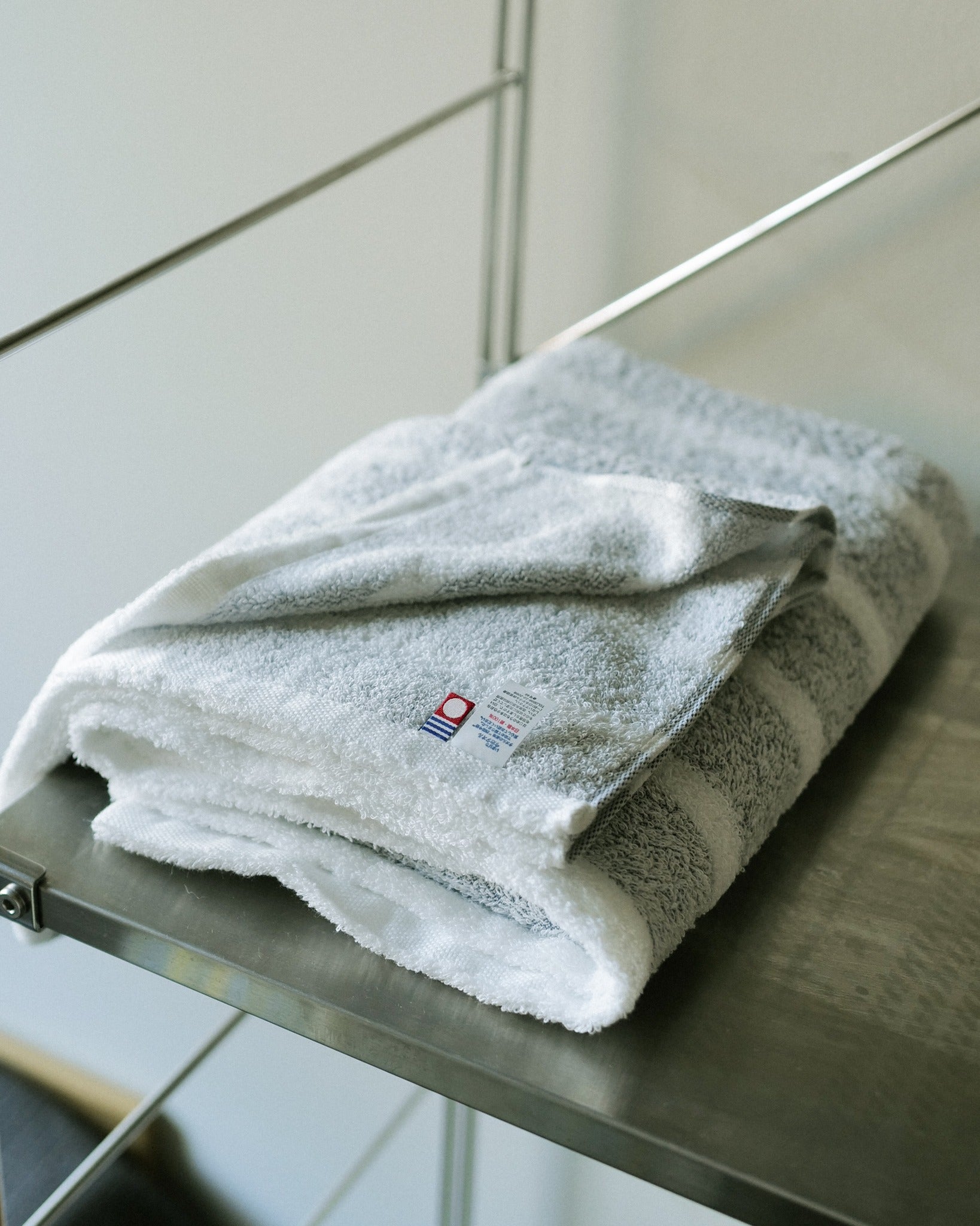 Grey striped Imabari towel folded on a steel shelf, showing the Imabari mark